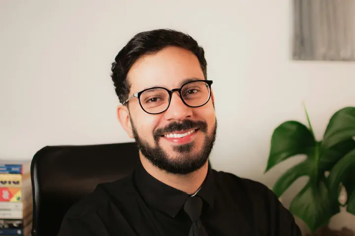 Thiago Heoli, de camisa e gravata, sorrindo no escritório dele
